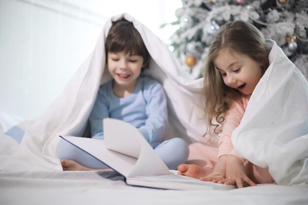 Una familia con niños divirtiéndose en la cama bajo las mantas durante las vacaciones de Navidad.