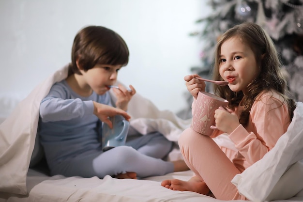 Una familia con niños divirtiéndose en la cama bajo las mantas durante las vacaciones de Navidad.