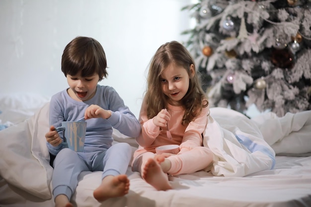 Una familia con niños divirtiéndose en la cama bajo las mantas durante las vacaciones de Navidad.