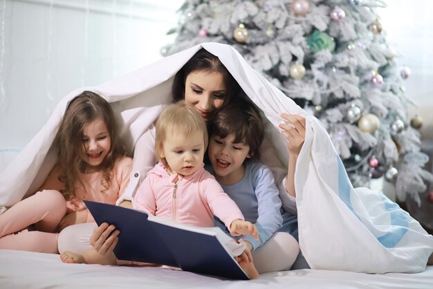 Una familia con niños divirtiéndose en la cama bajo las sábanas durante las vacaciones de Navidad