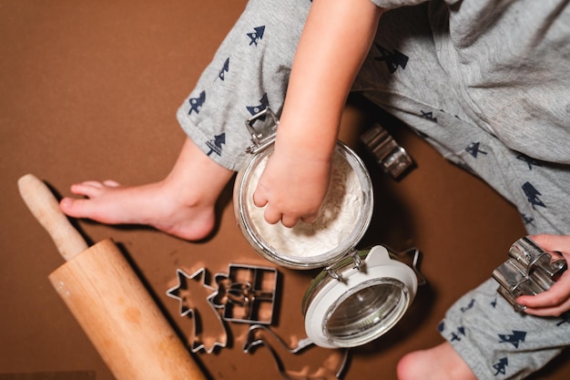 Familia con niños preparando galletas navideñas en la mesa espolvoreadas con harina