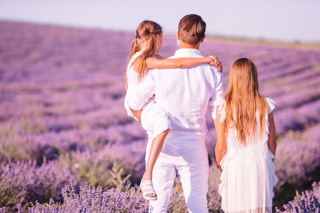 Família no campo de flores de lavanda ao pôr do sol em vestido branco e chapéu