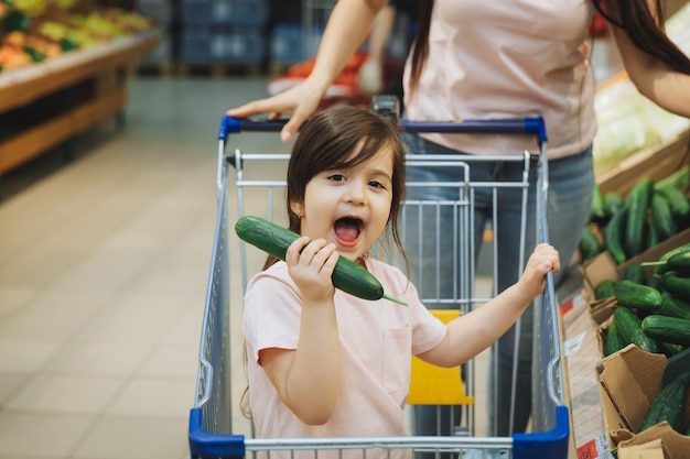 Foto família no supermercado jovem mãe e sua filha estão sorrindo e comprando comida conceito de comida saudável mãe e filha compram legumes e frutas no supermercado