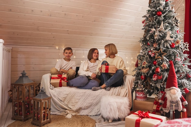 Familia en Nochebuena. Niños abriendo regalos. Niños bajo el árbol de Navidad con cajas de regalo. Habitación decorada de año nuevo. Acogedora y cálida noche de invierno en casa.