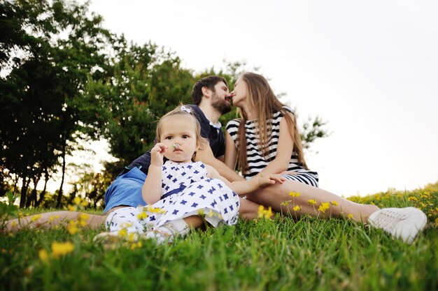 Família nova que relaxa no parque na grama. menina brincando na grama