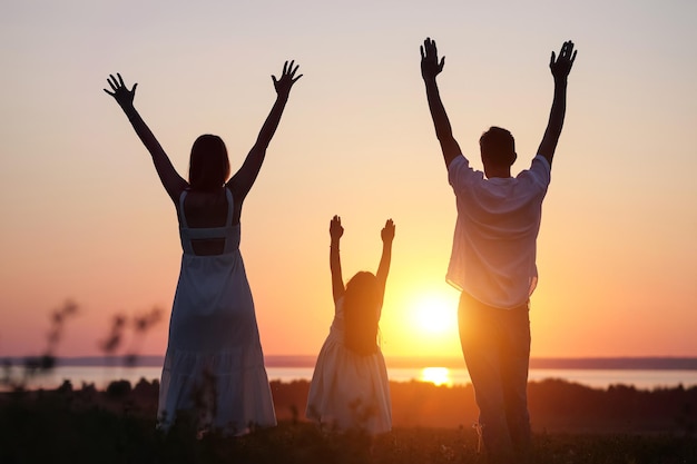 Família olha para o pôr do sol levantando as mãos para o céu no prado