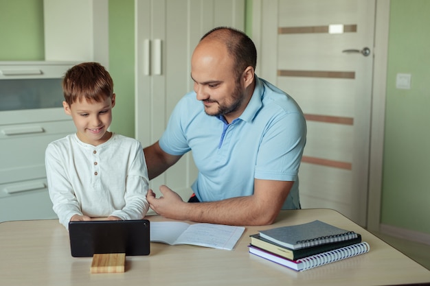 familia padre e hijo están sentados en una habitación en la mesa de la casa y haciendo la tarea usando una tableta.