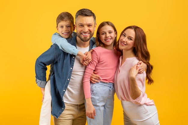 Foto familia con padre, madre y hijos abrazados en fondo amarillo