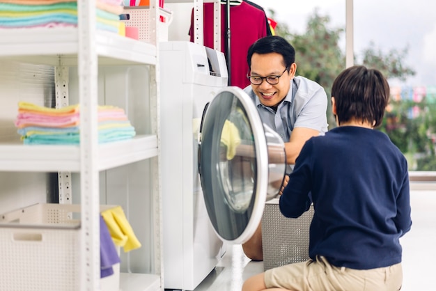 Família pai asiático e filho menino se divertindo fazendo tarefas domésticas, lavando roupas sujas na máquina de lavar roupa juntos na lavanderia em casa