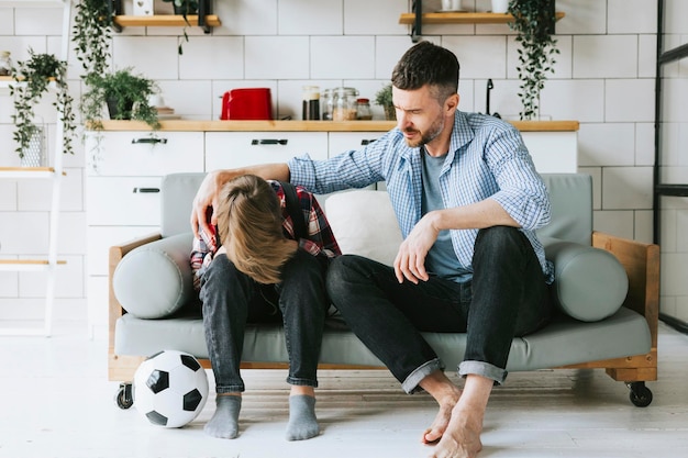 família pai jovem acalmar seu filho adolescente garoto bonito no sofá em um apartamento aconchegante bons momentos com sua família adolescente chateado perdendo no futebol