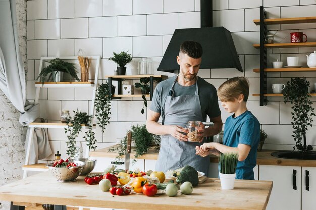 família pai jovem e filho adolescente cozinham salada de legumes na cozinha e passam bons momentos juntos pai e filho conversando e cozinhando comida vegetariana e fazendo tarefas domésticas 8 de março e dia das mães