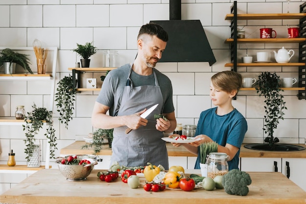 família pai jovem e filho adolescente cozinham salada de legumes na cozinha e passam bons momentos juntos pai e filho conversando e cozinhando comida vegetariana e fazendo tarefas domésticas 8 de março e dia das mães