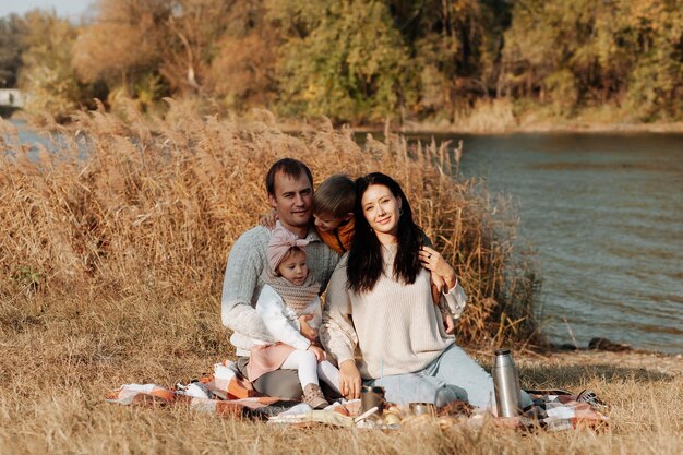 Familia en el parque de otoño. Mujer con un suéter blanco. Niños lindos con padres sentados en una manta junto al lago