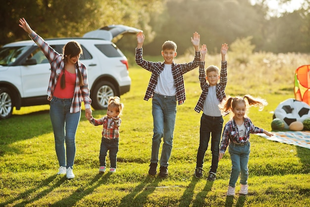 Familia pasando tiempo juntos Madre con cuatro hijos de pie y tomados de la mano contra un auto todoterreno blanco