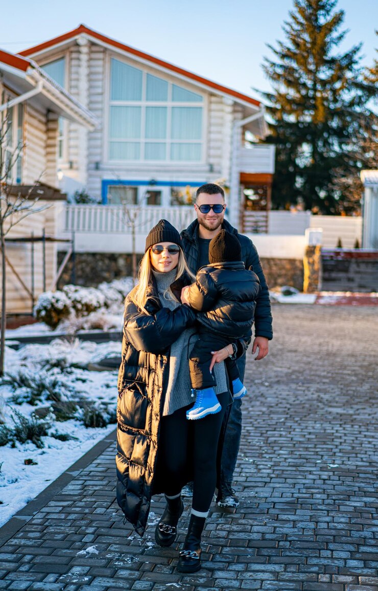 Familia en un paseo nevado Una familia camina juntos en una zona nevada vestidos cálidamente con una casa acogedora y árboles en el fondo