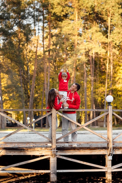 Familia en un paseo por el parque de otoño cerca del estanque. padre y madre tomados de la mano de su hija.