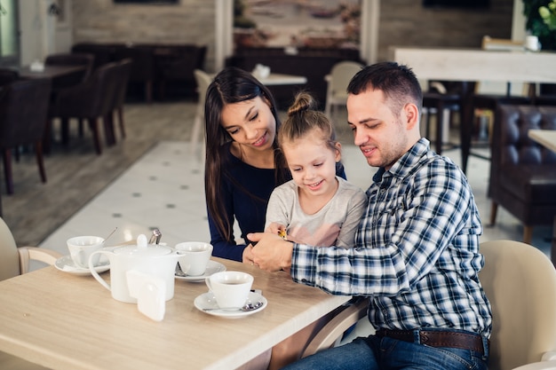 Familia, paternidad, concepto de personas de tecnología. feliz madre, padre y niña cenando tomando selfie por teléfono inteligente en el restaurante