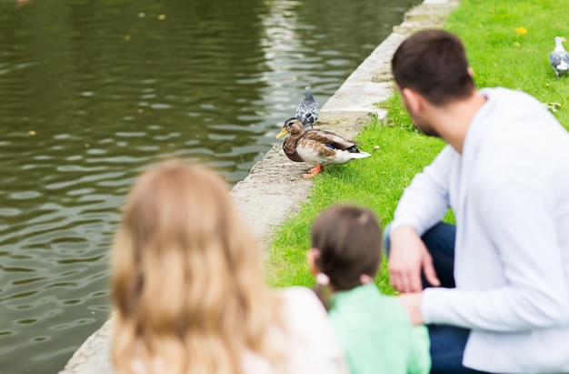 família, paternidade, lazer e conceito de pessoas - família olhando pato na lagoa de verão no parque