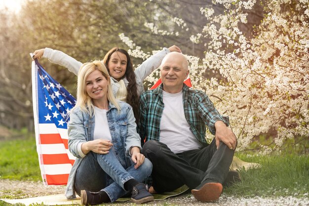 Familia patriótica sosteniendo la bandera de estados unidos al aire libre. Feliz pareja caucásica de edad avanzada sosteniendo la bandera de estados unidos en el fondo verde.
