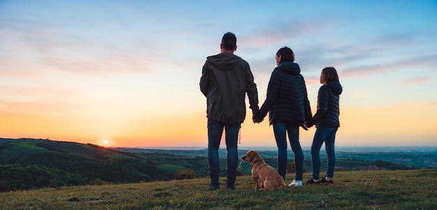 Familia con perro abrazando mientras está parado en la colina