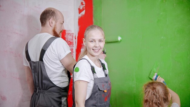 Família pintando paredes no novo apartamento na cor verde a mulher olhando para a câmera