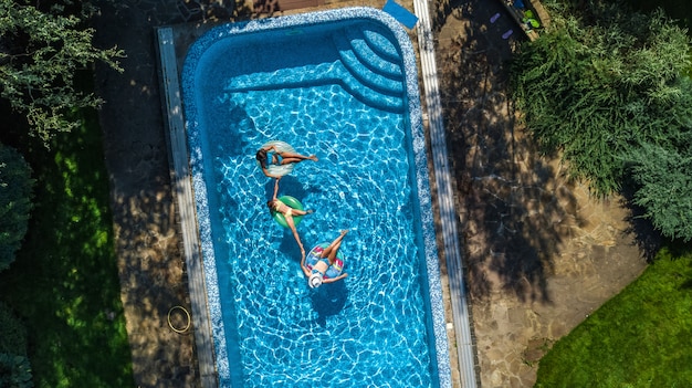 Familia en la piscina vista aérea de aviones no tripulados desde arriba, feliz madre e hijos nadan en anillos inflables y se divierten en el agua en vacaciones familiares, vacaciones tropicales en el resort