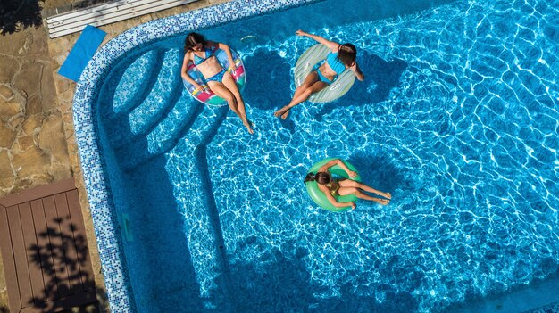 Familia en la piscina vista aérea de aviones no tripulados desde arriba, feliz madre e hijos nadan en anillos inflables y se divierten en el agua en vacaciones familiares, vacaciones tropicales en el resort