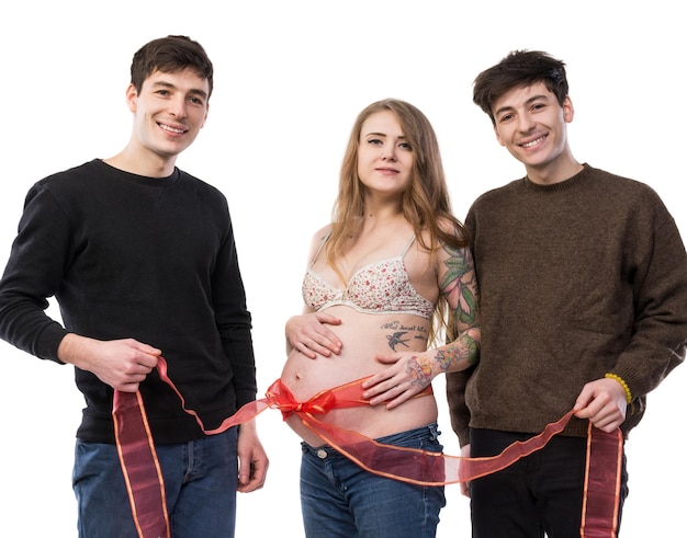 Família polígama moderna com uma esposa e dois maridos. Mulher grávida com fita vermelha na barriga posando com dois jovens em um fundo branco