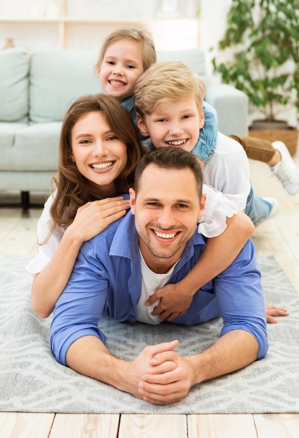 Familia Positiva De Cuatro Que Mienten Posando En El Piso En El Interior. Fin de semana juntos en casa. Vertical