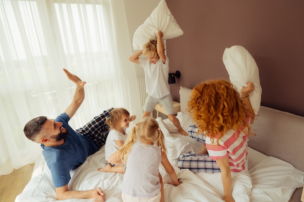 Família positiva encantada em uma batalha de travesseiros