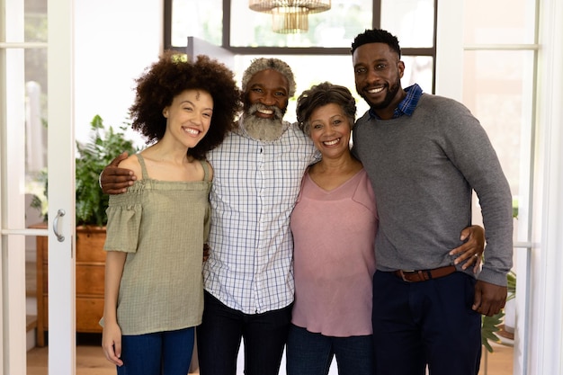 Familia de raza mixta disfrutando de su tiempo en casa juntos, de pie en un pasillo, abrazándose, mirando a la cámara y sonriendo