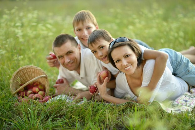 Familia recostada sobre la hierba cerca de la cesta de mimbre llena de manzanas