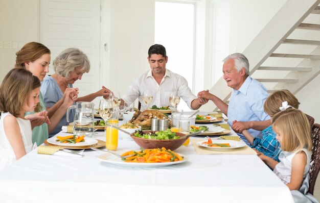 Familia rezando juntos antes de la comida en la mesa de comedor