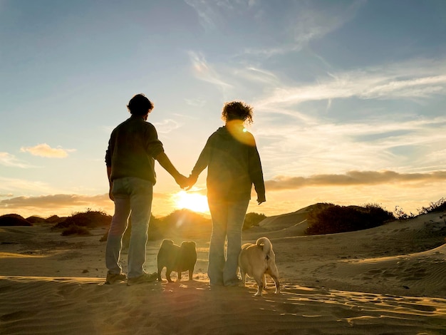 Família romântica com homem e mulher e dois cães admiram e desfrutam de um pôr do sol colorido em atividade de lazer ao ar livre Conceito de viagem e destino incrível para pessoas Casal apaixonado juntos e sol