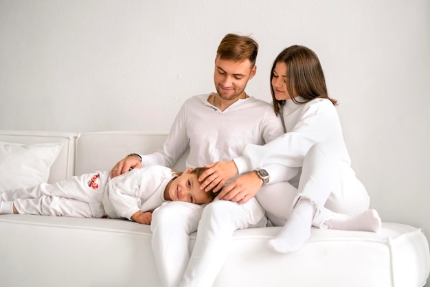 Una familia con ropa casual blanca está sentada en el sofá riendo alegremente juntos