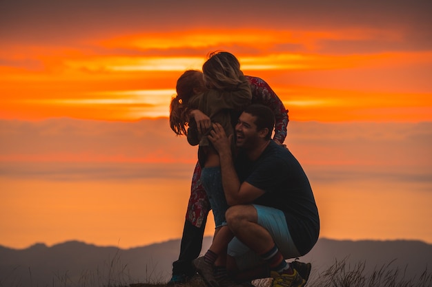 Família se abraçando no topo de uma montanha ao pôr do sol