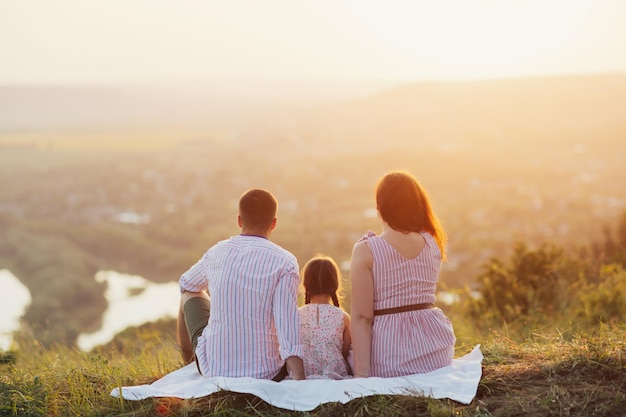 Familia sentada en la colina y disfruta del hermoso paisaje y la puesta de sol