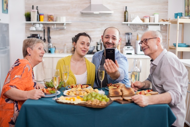 Familia sonriendo en videollamada mientras almuerza en la cocina. Esposa con esposo, madre y padre durante una llamada durante el brunch.