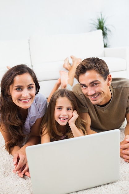 Foto familia sonriente acostada en una alfombra con la computadora portátil