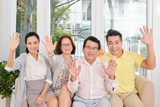 Familia sonriente de cuatro sentados en el sofá en casa y saludando con las manos