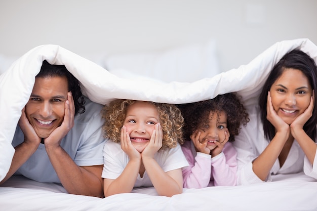 Familia sonriente escondida debajo de la manta