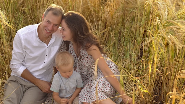 Familia sonriente feliz sentado en trigo en el campo