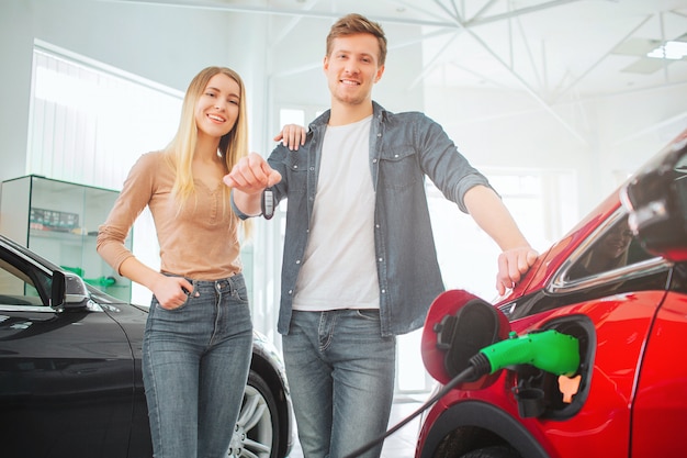 Familia sonriente joven que compra el coche eléctrico en la sala de exposición