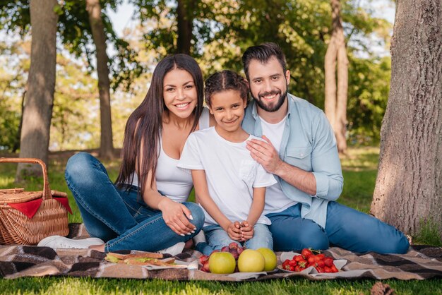 Foto familia sonriente mirando la cámara mientras pasan tiempo juntos en un picnic