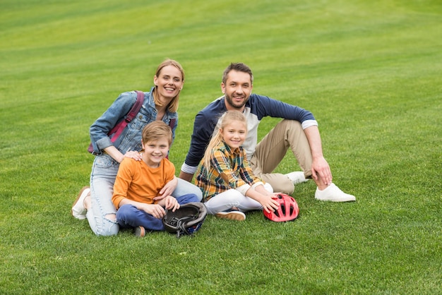 Foto familia sonriente mirando a la cámara mientras se sienta en el césped en el parque