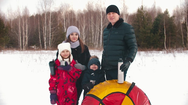 Familia sonriente de pie al aire libre en invierno con termos mirando a la cámara
