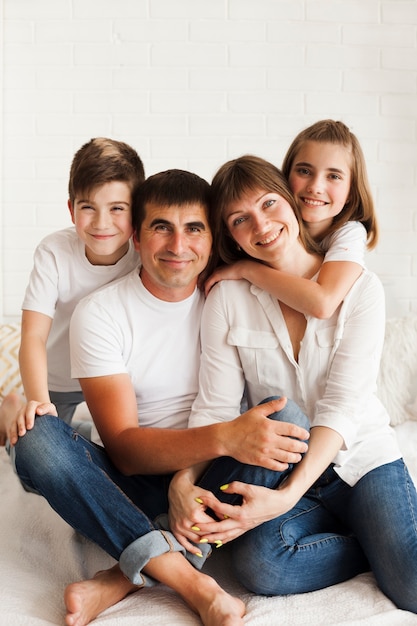 Familia sonriente que se sienta junto en cama y que mira la cámara