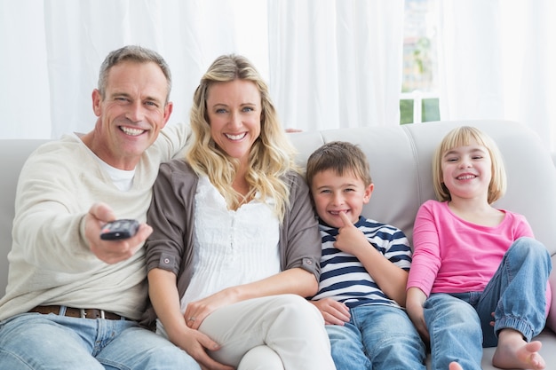 Familia sonriente sentada en el sofá cambiando el canal de televisión