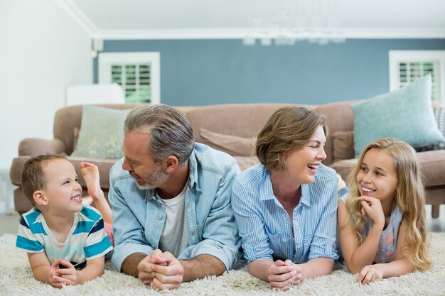 Familia sonriente tumbados juntos sobre una alfombra en el salón