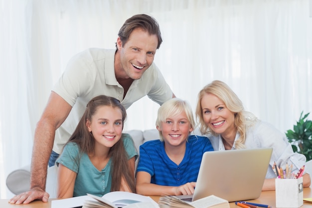 Familia sonriente usando la computadora portátil juntos para hacer la tarea